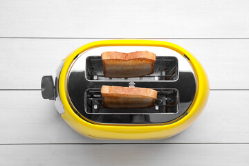 Yellow toaster with roasted bread on white wooden table, top view