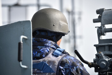 Fototapeta premium Navy soldier sitting at his machinegun post seen from behind