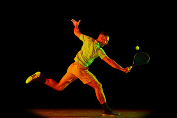 Obraz premium Young sportive man, professional tennis player in motion, action isolated over dark background in neon light. Concept of professional sport, competition, skills.