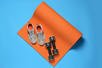 Exercise mat, dumbbells and shoes on turquoise background, flat lay