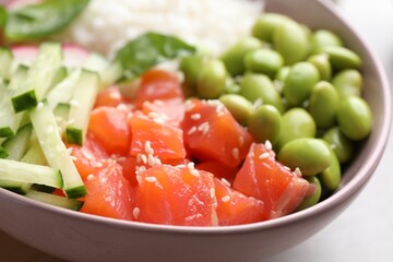 Poke bowl with salmon, edamame beans and vegetables on light grey table, closeup