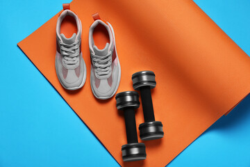 Exercise mat, dumbbells and shoes on turquoise background, flat lay