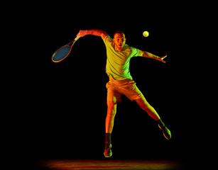 Fototapeta premium Dynamic portrait of energetic male tennis player in sportwear playing tennis isolated over dark background in neon light. Concept of motion, speed, professional sport.