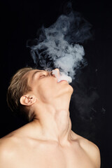 the man lets out fumes of smoke from his mouth throwing his head up