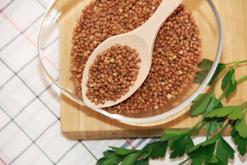 small grains of natural brown buckwheat in a wooden spoon and a glass plate
