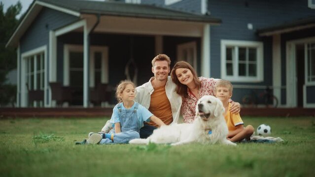Portrait of a Happy Young Family Couple with a Son and Daughter, and a Noble White Golden Retriever Dog Sitting on a Grass in Their Front Yard at Home. Cheerful People Looking at Camera and Smiling.