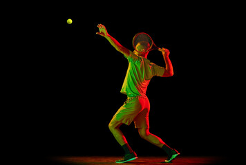 Dynamic portrait of energetic male tennis player in sportwear playing tennis isolated over dark background in neon light. Concept of motion, speed, professional sport.