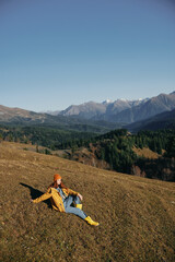 Fototapeta na wymiar Woman sitting full-length on a hill and looking out over the mountains happy nature trip on a hike in the autumn