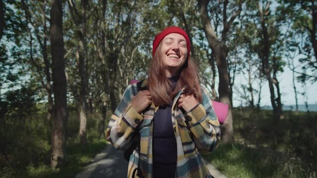 Portrait of young adorable female tourist laughing cheerful at camera enjoying sunny day in forest, travel lifestyle. Laughing backpacker woman having positive emotion during her hike.