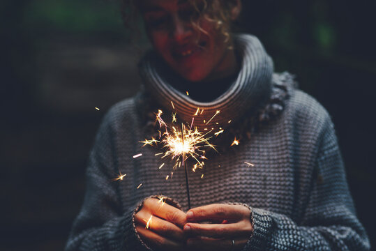 Woman celebration with sparkler light in the dark in outdoor leisure event activity. Happy female people holding sparkler in the forest. Green color. Concept of hope and new year celebration alone