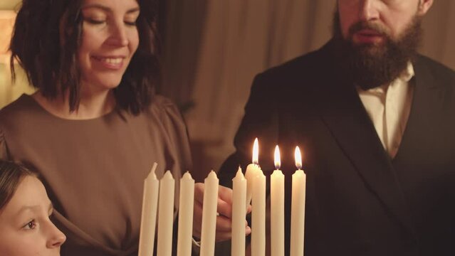 Jewish family of three gathering together to light menorah candles on Hanukkah celebrating it at cozy home in evening