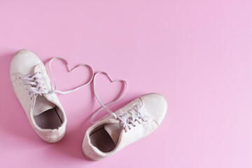 White leather sneakers isolated on pink background, Women's shoes, Fashionable casual shoes, Heart shape made of the shoelaces.