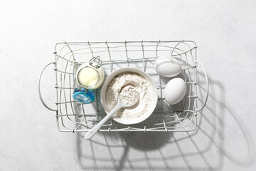 Fototapeta na wymiar Baking ingredients: flour, eggs, whisk, butter and milk on a white concrete background. Baking concept.