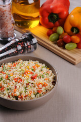 Couscous with vegetables in a rustic bowl surrounded by tomatoes, peppers and a glass of olive oil. Moroccan couscous. Selective focus.
