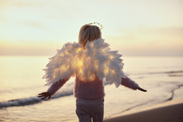 Cute little child girl standing on the sand beach near the sea during sunset with led glowing wings - 543183080