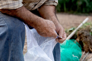 manos de campesino con navaja abriendo bolsa de bono en la huerta