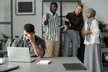 Middle aged Hispanic businessman sitting by workplace and networking against group of cruel...