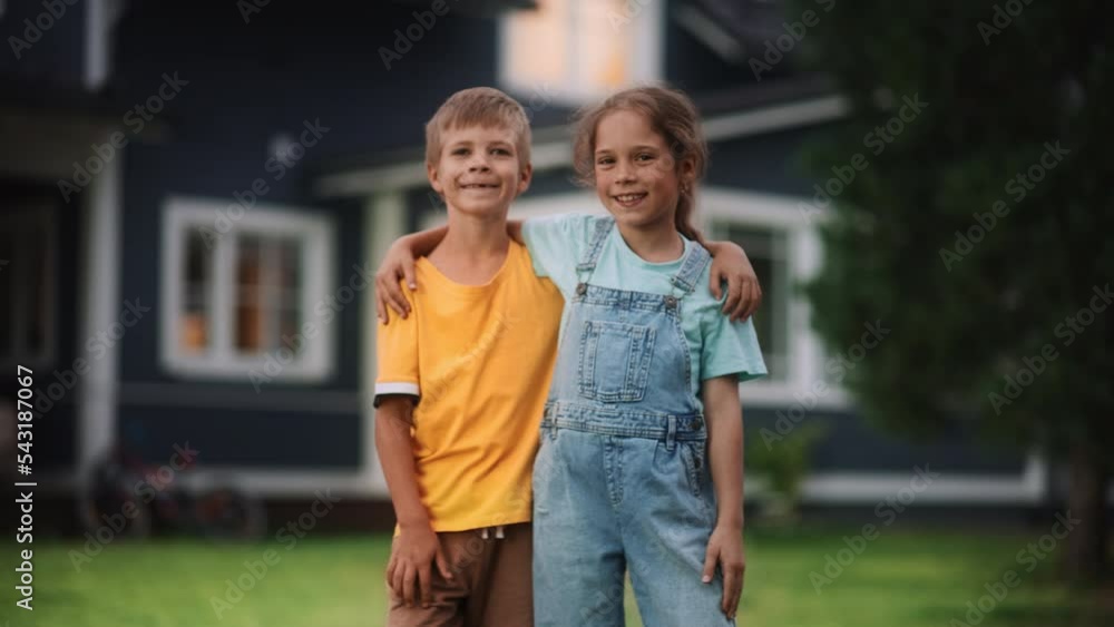 Wall mural Young Happy Brother and Sister Standing in Front of a Country House, Embracing Each Other, Looking at Camera and Smiling. Two Kids Enjoying Childhood and Friendship.