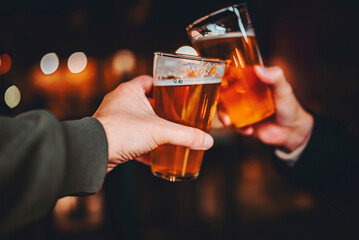 Two friends hands toasting with glasses of craft beer at the pub or bar.