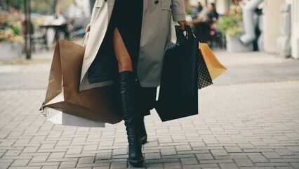 4k woman walks with shopping bags in the old city. Female in coat walking in autumn sunny day. Glamour lady.