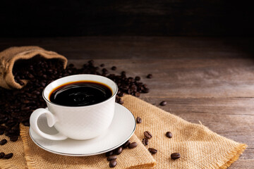 A hot coffee cup was Placed on an old wooden table on a black background, the soft sunlight shone into a warm atmosphere.