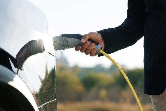 Close up of unrecognizable man disconnecting an electric vehicle from charging station. Charging of electric car. Male hand unplugs power connector into EV car. Concept of green energy.
