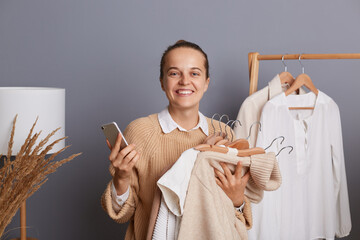 Photo of extremely happy woman shopper holding clothes on racks in modern boutique, choosing new...