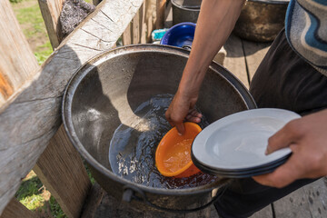 Ukrainian male farmer washes dishes with clean water in the farm yard , closeup, outdoors. Rural...