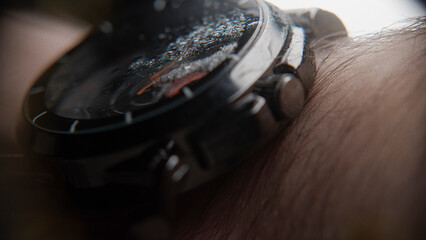 Extreme close-up of blurry looking wristwatch with water particles, wearing on the arm, background...