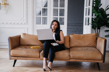 Overloaded Brazilian businesswoman working home sitting on cozy leather sofa using laptop. Tired African American entrepreneur making video call. Beautiful hispanic woman remote studying. Education.