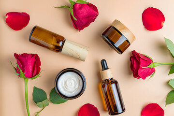 Obraz na płótnie Canvas Set of natural organic SPA beauty products on beige background with red roses and petals. Homemade rose face oil, moisturizer cream jar, amber glass spray bottle on beige background