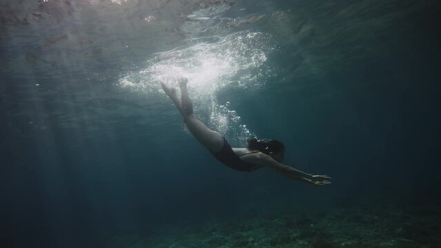 Slow motion close up shot of girl in swimming body suit swimming underwater air bubbles coming out of her nose