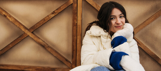 Pleasant young caucasian woman looking at camera sits outdoor during winter holidays. Brunette wears sweater and jacket. Concept leisure time, lifestyle.