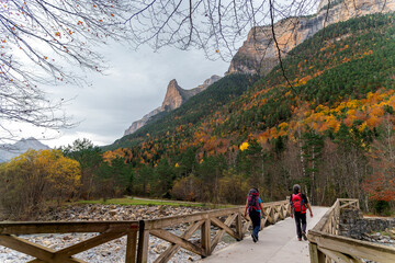 A couple of hikers walk along a path in the Ordesa-Monte Perdido National Park, in the Pyrenees mountains (Spain), in the autumn season.