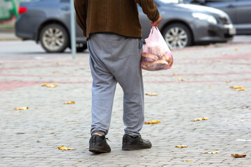 Obraz premium homeless poor man walks down the city street with a bag in his hand. social problems of the city and people