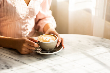 A woman's hand holds a cup of coffee with latte art on the table. in the window cafe.