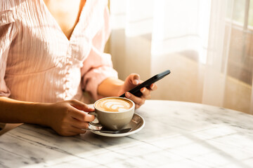 Portrait of a woman holding a cell phone and a white latte cup on a table in a modern cafe.