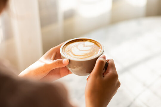 A woman's hand holds a cup of coffee with latte art on the table. in the window cafe.