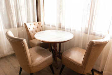 Leather-upholstered chairs and a round wooden table covered in marble near a bright window. retro style cafe decoration
