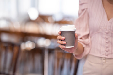 Woman holding a hot cappuccino in a white paper cup in a cafe