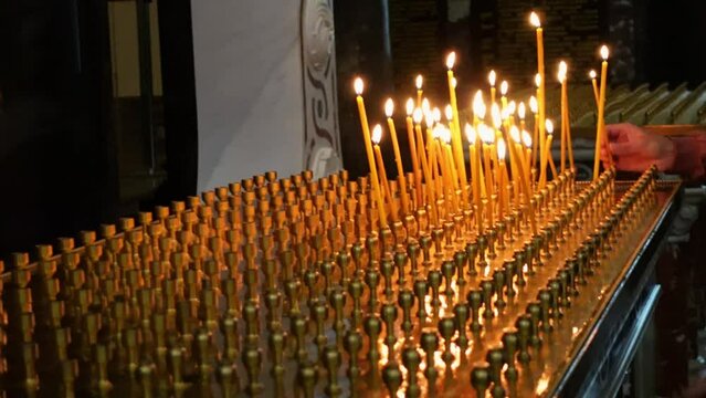 People put burning votive candles in candlesticks in church as sign of their faith and hope in help of God, side view, close up. People pray for health or for the repose.