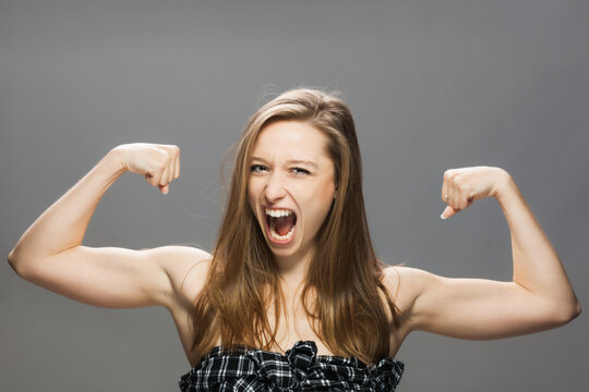 Skinny Brunette Girl Showing Muscles And Screaming. Studio Portrait Against Gray Background...