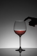 Woman posing her finger on the rim of the glass of red wine. Black silhouette.