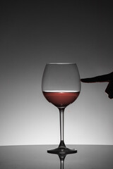 Woman pushing the glass of red wine with her finger. Black silhouette.