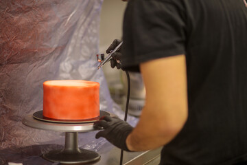 pastry chef designer using edible red paint airbrush to spray frosted cup cake