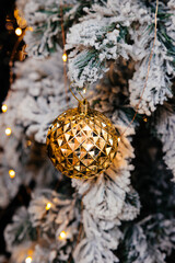 Christmas toy of gold color against the background of artificial spruce branches covered with artificial snow