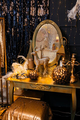 gold color dressing table decorated with feathers, candelabra, gold color lanterns in a room with black walls decorated with gold garlands