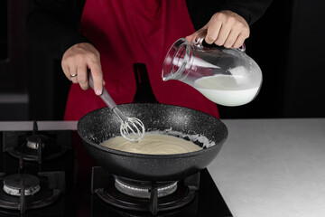 Chef cook making white cheese sauce for mac and cheese meal. Ingredients: Milk, cheese, flour and butter in wok pan on kitchen gas stove.
