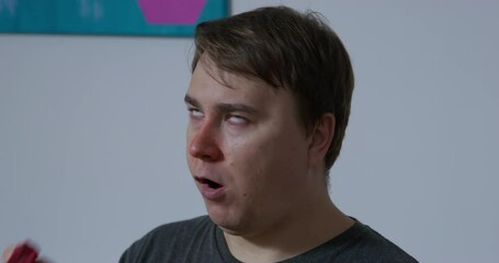 Portrait of a strange young man with a red nose, who eats a thread and then tries to chew a sock while in a trance, front view. Person suffers from sleepwalking.
