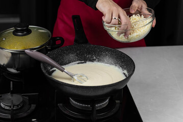 Chef cook making white cheese sauce for mac and cheese meal. Ingredients: Milk, cheese, flour and butter in wok pan on kitchen gas stove.